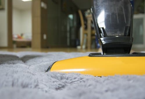 Who Invented the Vacuum Cleaner? Person vacuuming a gray rug